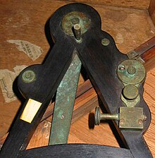 Octant reverse side. This side is not seen in photographs very often. On the right, the thumbscrew to adjust the horizon mirror can be seen. At the top, one of the feet on which the octant rests in its case is just below the index arm axis. On the left the notepad is clearly visible. This small keystone-shaped piece of ivory, scarcely larger than a thumbnail, was used by the navigator to record his readings. Octant-notepad.jpg