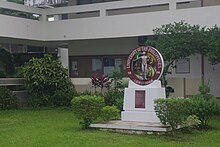 Tacloban College, Tacloban, Philippines. There is a green lawn in front of a white building, with a sign reading "UNIVERSITY OF THE PHILIPPINES 1908 - 2008 CENTENNIAL" in front.