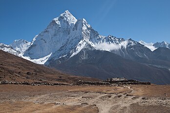 Vista da montanha Ama Dablam na cordilheira do Himalaia oriental. O pico principal é de 6 812 metros, o pico ocidental inferior é de 6 170 metros. Ama Dablam significa “colar da mãe”; as longas cristas de cada lado como os braços de uma mãe (ama) protegendo seu filho, e a geleira suspensa considerada como o dablam, o tradicional pingente duplo contendo imagens dos deuses, usado por mulheres xerpas. Durante vários dias, Ama Dablam domina o céu oriental para quem faz a trilha até o Campo Base do Everest. Por seus cumes elevados e faces íngremes, Ama Dablam é às vezes referida como o “Matterhorn dos Himalaias”. (definição 4 032 × 2 688)