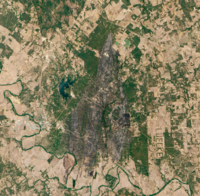 Satellite image of the burn scar, which appears as large blackened area within green forests using data that approximates human vision