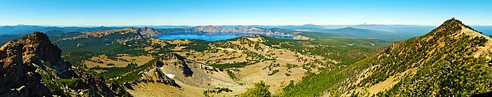 Panorama depuis un sommet vers la caldeira et son lac, dans un paysage d'éboulis, de pelouses alpines et de forêts.