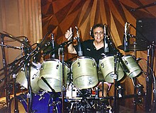 Blaine sitting behind a large drum set giving a thumbs up