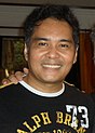 An image of John Arcilla in a black shirt smiling to the camera