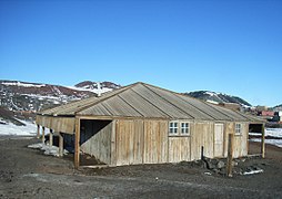 Cabane en bois avec en fond une station de recherche antarctique.