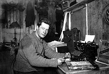 Photographie noir et blanc d'un homme assis à un bureau devant une machine à écrire.