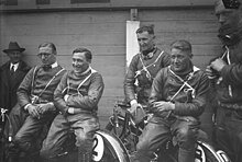 Photo de quatre hommes en tenue de pilote moto, assis sur leurs deux-roues.