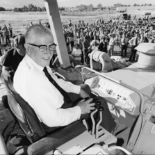 An older man in a shirt and tie sits in a bulldozer