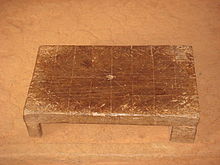 прямоугольный деревянный табурет с вытравленными на поверхности линиями в четыре ряда