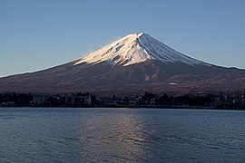 Volcan conique, au sommet enneigé, surmontant une agglomération au bord d'un lac.