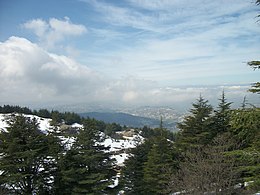 Skyline of rolling hills of pine forests, some covered by snow, with small village in the backdrop