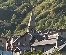 Photographie d'un clocher d'église et des maisons aux toits gris, en tôles ou en pierres, au centre d'un village.