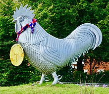 The sculpture, facing left, wearing a gold medal labeled "London 2012" with a red and blue knitted ribbon