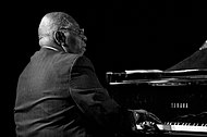 Photographie en noir et blanc d'un homme de dos qui joue du piano.