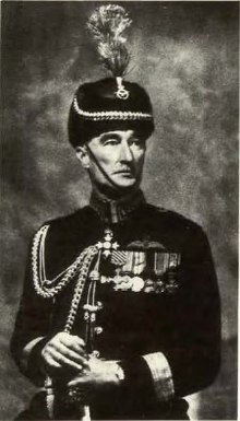 Portrait formel d'un homme en uniforme de couleur foncée et coiffé d'un galon et de médailles.