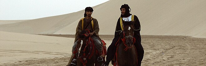 Photo panoramique de deux cavaliers dans le désert.