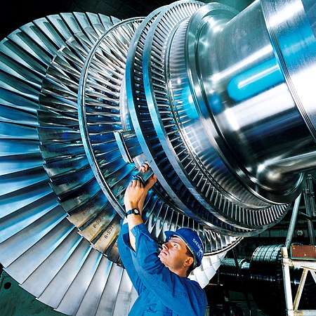 在德国的一家西门子工厂中，一名工人正在给一个蒸汽涡轮发动机的转子安装涡轮叶片。