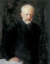 A middle-aged man with grey hair and a beard, wearing a dark suit and staring intently at the viewer