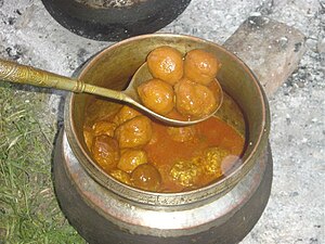 A metal pot is filled with an orange-brown sauce and meatballs.