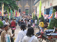 Le parvis est pavoisé de fanions multicolores. Au fond près de la pagode, on devine les échoppes vendant de la nourriture, des fleurs de lotus, de l'encens, etc.