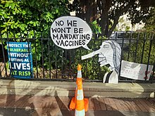 Anti-government sign attached to a railing states, "No, we won't be mandating vaccines", with a caricature of Ardern sporting a Pinocchio nose.