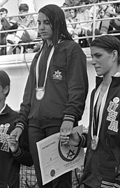 פודיום 100 מטר חופשי לנשים ביום הראשון לתחרויות. המנצחת, מורין קפלן מדרום אפריקה. במקום השני, ננסי ספיץ. שימו לב לאוזן שלה: מאורכת כלפי מטה וללא עגיל.[4]