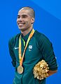 Sportif au crâne rasé et aux bras atrophiés, souriant avec une médaille d'or autour du cou.