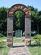 A brick and sandstone arch frames a green sign in the background in a grassy field