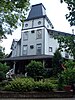 Grey clapboard tower surrounded by shrubbery