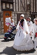 Une femme, maquillée d'un rouge à lèvres grossièrement appliqué et habillée d'une robe de mariée et d'une écharpe de miss, défile dans la rue.