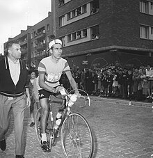 Photographie en noir et blanc montrant un cycliste sur son vélo, un homme se tenant à côté.