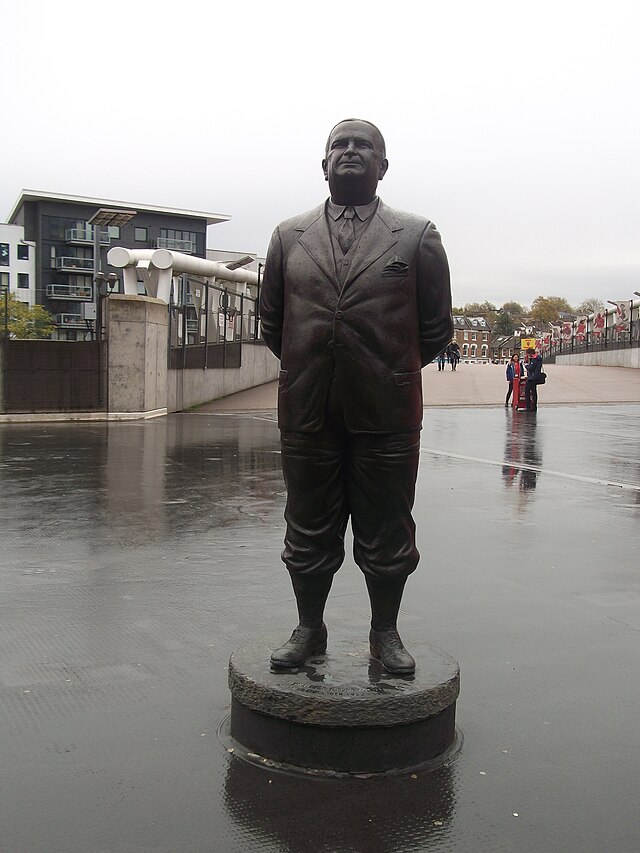 A bronze-statued Herbert Chapman, standing with hands behind his back. The statue was erected to commemorate his time at Arsenal.