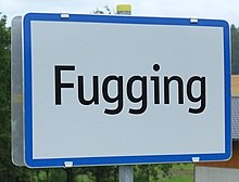 A road sign for the town of Fugging. The sign simply says "Fugging", and has a blue rectangular border around a white background, with the black text of the town name.