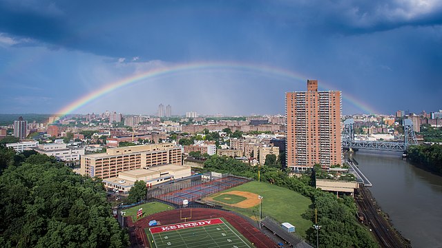 Uma visão geral de Marble Hill, vista do oeste. O campus educacional John F. Kennedy é visível em primeiro plano, e o resto do bairro está no centro, delimitado pelo rio Harlem no lado direito. O Bronx está em segundo plano.