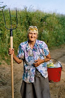 photo d’une femme sur un chemin terreux tenant une fourche et un seau