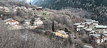 Photographie de bâtiments plus ou moins uniformes avec des lauzes ou de la tôle grise au toit ainsi que des murs en pierres, blancs ou encore en bois, répartis en différents groupements dans la montagne.