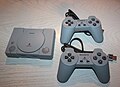 A PlayStation Classic console next to its USB controllers.