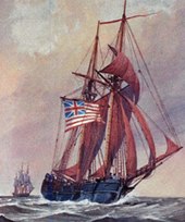 A two-masted wooden sailing ship is shown in full sail on the sea. It is flying the flag of the United Colonies: thirteen red and white stripes, with a British Union Jack in the upper left quadrant. Another ship is visible in the distance.