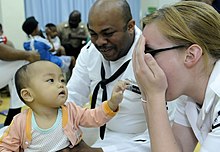 Angkatan Laut AS 100406-N-7478G-346 Spesialis Operasi Kelas 2 Reginald Harlmon dan Teknisi Elektronik Kelas 3 Maura Schulze bermain cilukba dengan seorang anak di Bangsal Anak-anak di Rumah Sakit Likas