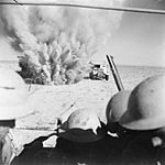 A mine explodes close to a British artillery tractor as it advances through minefields at the Second Battle of El Alamein. A mine explodes close to a British truck as it carries infantry through enemy minefields and wire to the new front lines.jpg