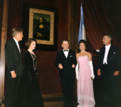 Three men and two women stand near the Mona Lisa. All are dressed formally, one woman in a spectacular pink gown.