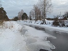 Drewniane domy pokryte śniegiem w pobliżu cieku wodneg częściowo skutego lodem