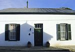 Single storey with double pitched roof and bargeboard. Symmetrical three bay facade. Sooth opening surrounds. Low stoep. 6x6 double sliding sash windows with louvred shutters. 4-panel door under 3-pane fanlight. Good condition. Well restored to original Land first surveyed, and transferred in 1862. Type of site: House Current use: Residential : House. This house is representative of early Karoo architecture. It is square with a beautiful cornice and interesting fan- light above the door.