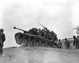 Men sit on a tank which is holding position among a line of troops