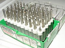 A box of drill bits used for making holes in printed circuit boards. While tungsten-carbide bits are very hard, they eventually wear out or break. Drilling is a considerable part of the cost of a through-hole printed circuit board. Box of 02in pcb bits.jpg