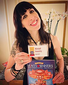 Author Margot Douaihy posing with ID card and a catalog at the New Orleans Saints & Sinners LGBTQ+ Literary Festival in 2023.