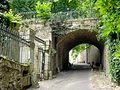 Arche large en pierres appareillées, avec rambarde en fer forgé, enjambant une rue étroite.