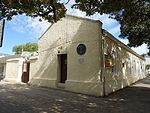 Single storey – single pile plan. Corrugated iron roof. Rough plaster to walls. Sash windows with raised margins. Thich walls to back and side. Like most of the cities and towns of South Africa, Grahamstown grew from modest beginnings. A simple, elongated building in High Street, not far from the Drostdy gateway was one of the first buildings to arise in the town, if indeed it was not the first. Type of site: Gaol Current use: Old Gaol. The erection of the old gaol was commenced in 1813, shortly after the founding of Grahamstown (1812). In 1814 one of the walls of the gaol served as a line for the surveying of the main street, and thus also as the basis for the layout of the whole town.