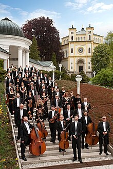 Západočeský symfonický orchestr v Mariánských Lázních, v pozadí kostel Nanebevzetí Panny Marie