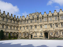 Правильный узор окон и фронтонов с двух сторон четырехугольника зданий; на снегу видны совпадающие тени фронтонов на стене позади фотографа