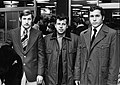 Photographie en noir et blanc de trois joueurs de football, habillés dans un manteau, vus de face.